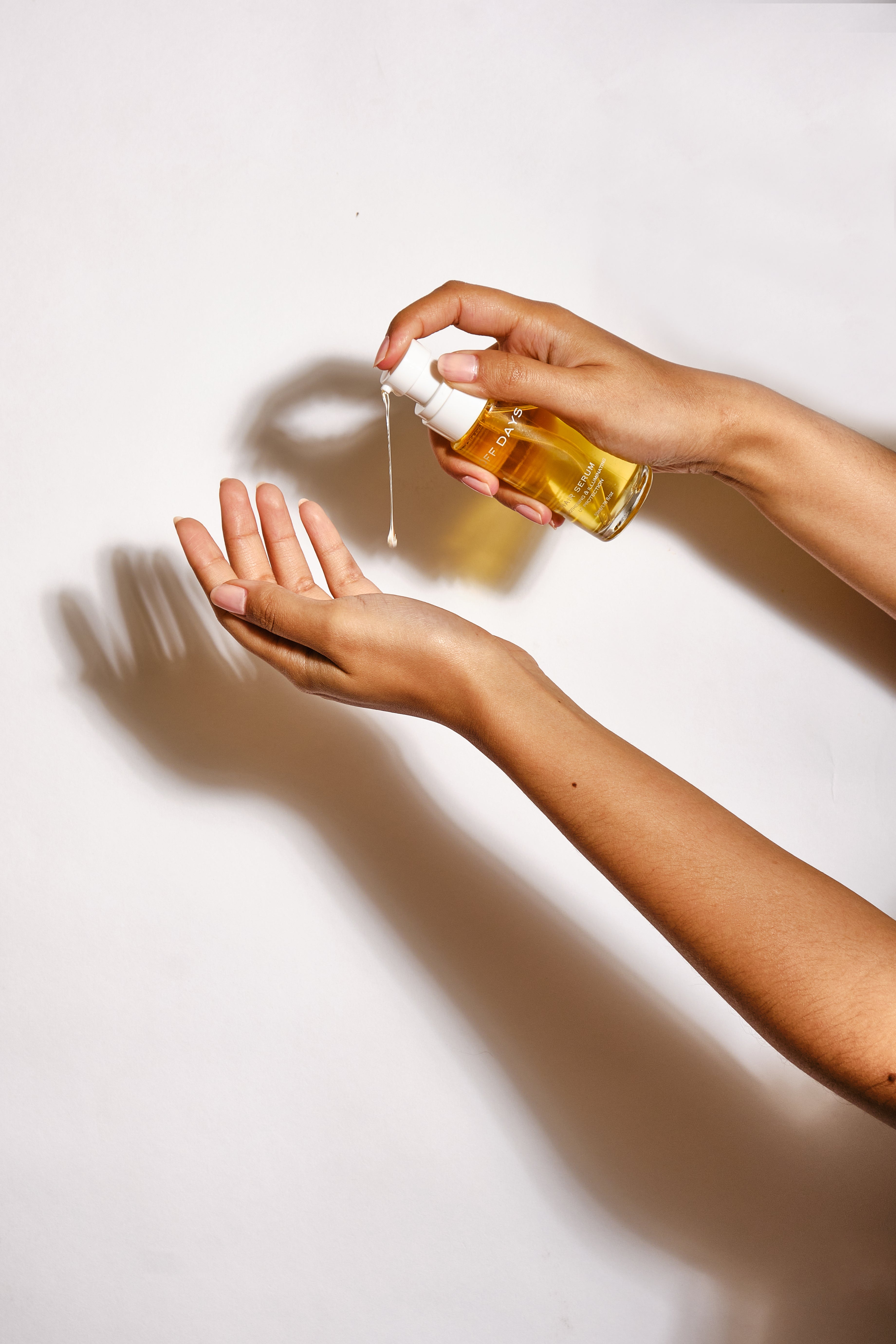 Hands holding the hair serum lightly squeezing out a small amount into her hand. Golden hue of the product